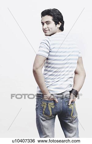 Rear view of a young man standing with his hands in his pockets View Large Photo Image Stock Photograph - Rear view of a young man standing with his hands in his pockets. Fotosearch