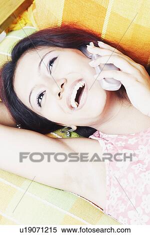 Close-up of a young woman lying down and talking on a mobile phone View Large Photo Image Stock Photography - Close-up of a young woman lying down and talking on a mobile phone. Fotosearch