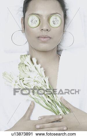 Stock Image - High angle view of a young woman with cucumber slices on her eyes. Fotosearch