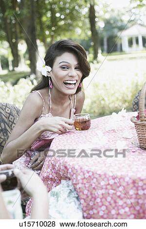 Stock Photo - Portrait of a young woman holding a cup of tea sitting at a table. Fotosearch
