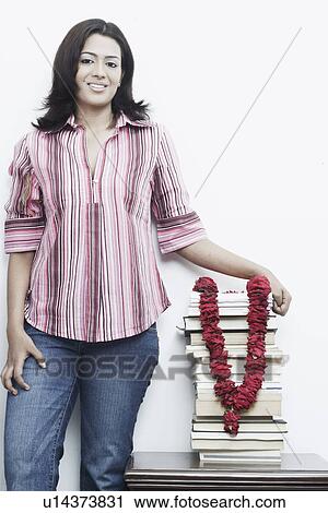 Stock Image - Portrait of a young woman standing with a stack of books on the table. Fotosearch