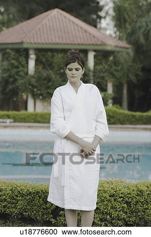 Stock Image - Young woman with a facial mask standing at the poolside. Fotosearch