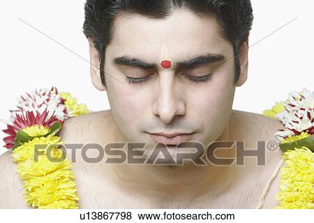 Stock Photo - Close-up of a young man with his eyes closed wearing a garland. Fotosearch