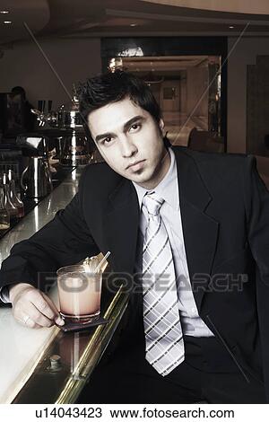 Stock Image - Portrait of a businessman sitting at a bar counter with a cocktail. Fotosearch