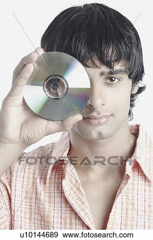 Portrait of a young man holding a compact disk in front of his face View Large Photo Image Stock Photo - Portrait of a young man holding a compact disk in front of his face. Fotosearch