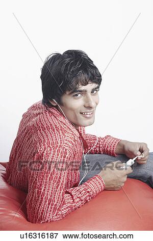 Stock Photo - Portrait of a young man sitting on a bean bag and listening to music. Fotosearch