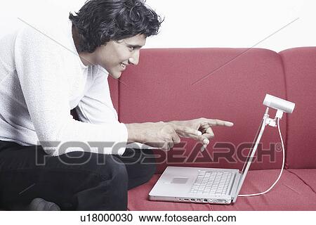 Side profile of a young man sitting on a couch in front of a laptop View Large Photo Image Stock Image - Side profile of a young man sitting on a couch in front of a laptop. Fotosearch
