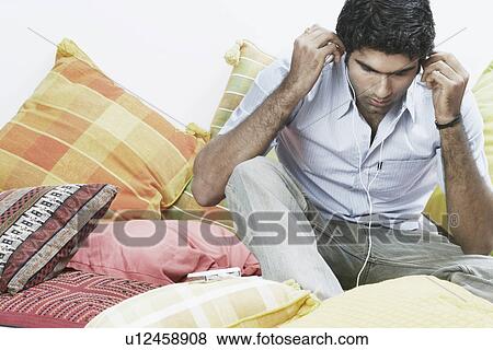 Young man sitting and listening to an MP3 player View Large Photo Image Stock Photo - Young man sitting and listening to an MP3 player. Fotosearch