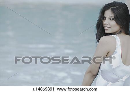 Stock Image - Portrait of a young woman sitting at the poolside. Fotosearch