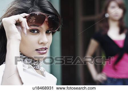 Stock Image - Side profile of a young woman holding her sunglasses on her forehead. Fotosearch