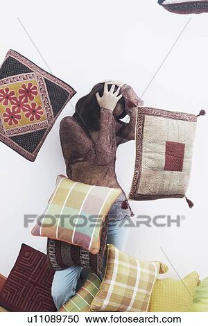 Stock Image - Young woman protecting herself from flying cushions. Fotosearch