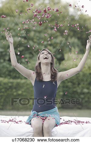 Stock Image - Young woman throwing rose petals in the air. Fotosearch