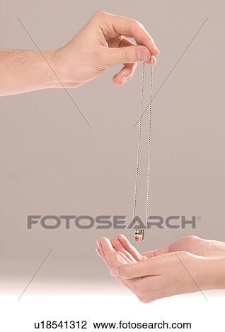 Stock Image - Close-up of a man's hand putting a chain in a woman's hand. Fotosearch