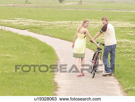 Stock Image - Rear view of a young couple walking with a cycle. Fotosearch