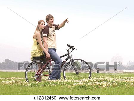 Stock Image - Side profile of a young couple sitting on a cycle. Fotosearch