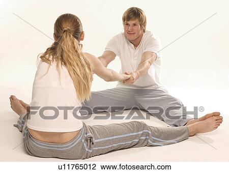 Stock Image - Young woman exercising with a young man on the floor. Fotosearch