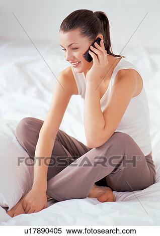 Stock Photography - cell, bedroom, one person, smiling, pillow, holding, wireless. Fotosearch