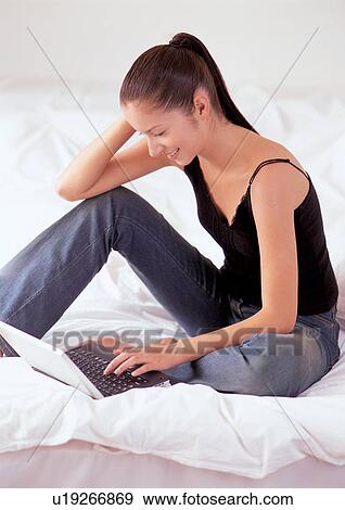 Stock Photo - hands on keyboard, bed, quilt, bed sheet, cushion, night dress, young woman. Fotosearch