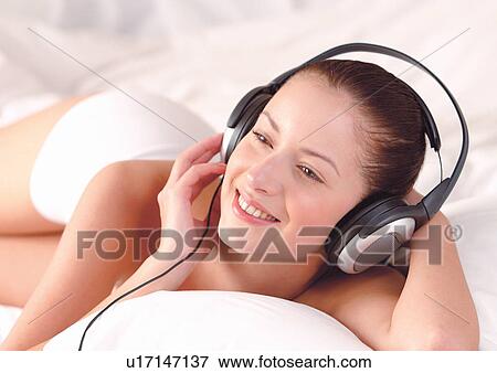 Stock Photo - lying down, indoor, listening, music, phones, bedding. Fotosearch