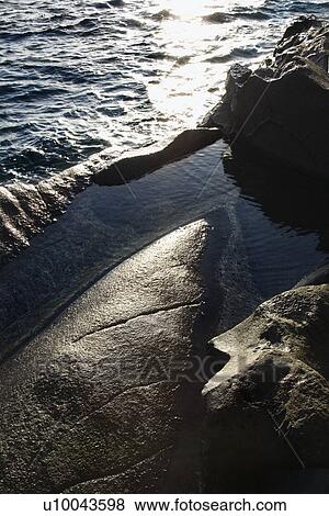 Stock Photo - Big rocks on coast with lapping water.. Fotosearch