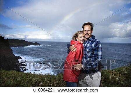 Stock Image - Caucasian couple embracing with rainbow in background in Maui Hawaii. Fotosearch