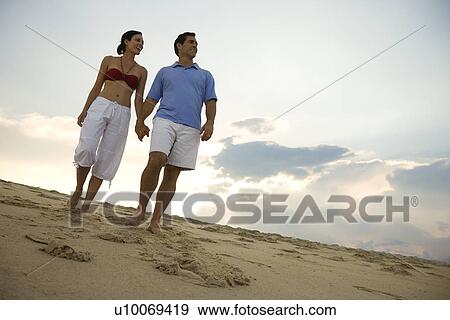 Stock Photo - Caucasian mid-adult couple holding hands walking on beach.. Fotosearch