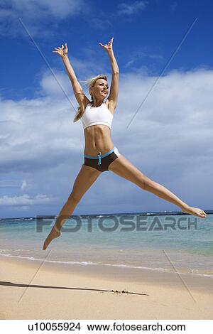 Picture - Caucasian young adult woman jumping on beach.. Fotosearch