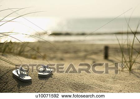Stock Image - Two white sandals on sandy beach with ocean in background.. Fotosearch