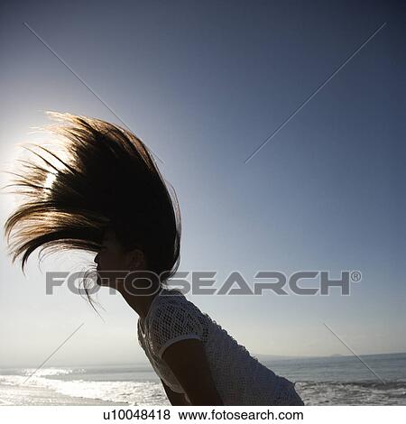 Stock Photo - Young Asian female swinging her hair back at the beach with sun in background.. Fotosearch