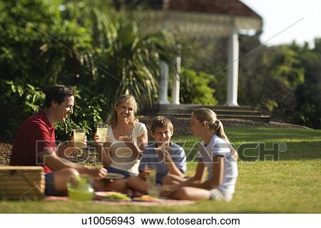 Stock Image - Caucasian family of four having picnic in park.. Fotosearch