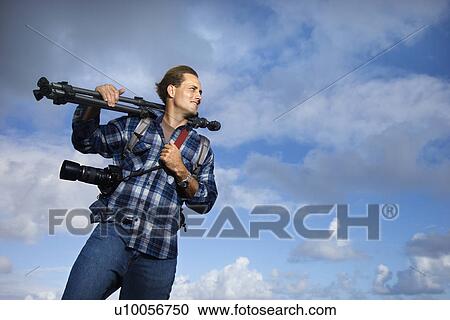 Caucasian mid-adult man standing with camera and tripod over his shoulder. View Large Photo Image Stock Image - Caucasian mid-adult man standing with camera and tripod over his shoulder. . Fotosearch