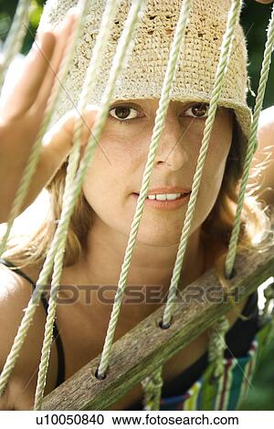 Stock Image - Caucasian mid-adult woman looking through hammock.. Fotosearch