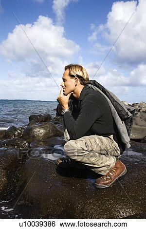 Caucasion mid-adult man kneeling on rocky coast looking at ocean in Maui, Hawaii. View Large Photo Image Stock Photograph - Caucasion mid-adult man kneeling on rocky coast looking at ocean in Maui, Hawaii.. Fotosearch