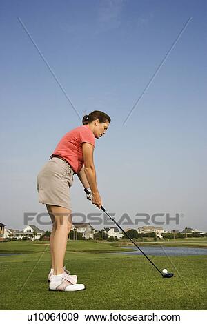 Stock Photo - Caucasion mid-adult woman preparing to drive golf ball.. Fotosearch