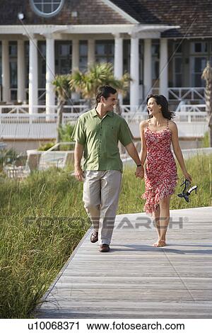 Stock Image - Mid-adult Caucasian couple holding hands walking down wooden trail. . Fotosearch