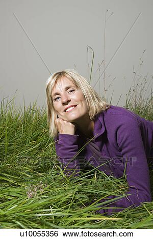 Middle-aged Caucasian woman lying in grass resting head on hand smiling. View Large Photo Image Stock Photograph - Middle-aged Caucasian woman lying in grass resting head on hand smiling.. Fotosearch