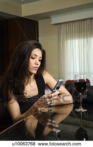 Prime adult Hispanic female sitting at bar looking at cellphone. View Large Photo Image Stock Photo - Prime adult Hispanic female sitting at bar looking at cellphone.. Fotosearch