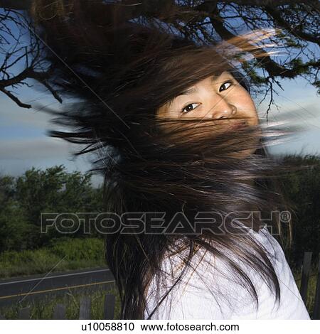 Stock Image - Young adult Asian female looking at viewer and swinging her hair.. Fotosearch