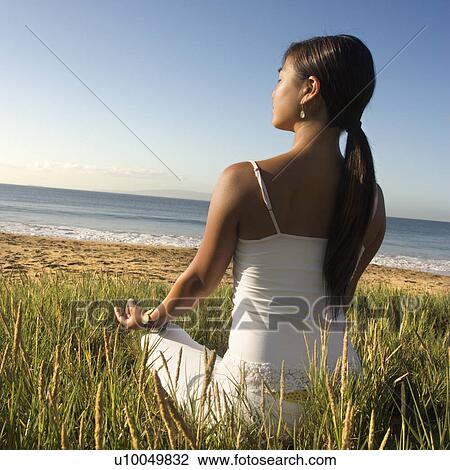 Young Asian female sitting on beach meditating and looking out to ocean. View Large Photo Image Stock Image - Young Asian female sitting on beach meditating and looking out to ocean.. Fotosearch
