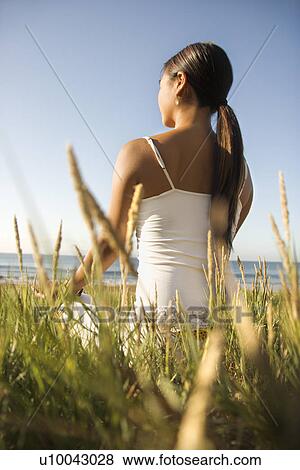 Stock Photo - Young Asian female sitting on beach looking out to ocean.. Fotosearch