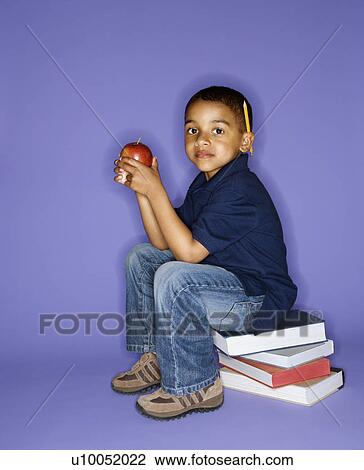 Stock Image - African American male child sitting on stack of books.. Fotosearch