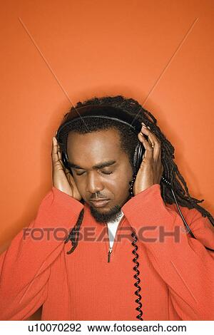 African-American mid-adult listening to headphones wearing orange clothing on orange background. View Large Photo Image Stock Image - African-American mid-adult listening to headphones wearing orange clothing on orange background.. Fotosearch