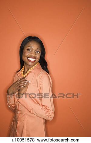 Stock Photo - African-American mid-adult woman on orange background wearing orange clothing.. Fotosearch