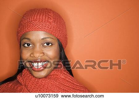 Stock Photo - African-American mid-adult woman wearing orange scarf and hat on orange background.. Fotosearch