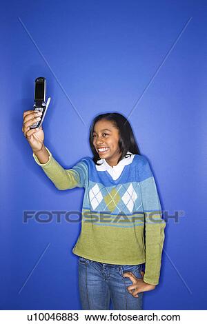 Portrait of African-American teen girl taking photo with camera phone standing in front of blue background. View Large Photo Image Stock Image - Portrait of African-American teen girl taking photo with camera phone standing in front of blue background.. Fotosearch