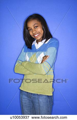 Stock Photo - Portrait of African-American teen girl with arms crossed standing against blue background.. Fotosearch