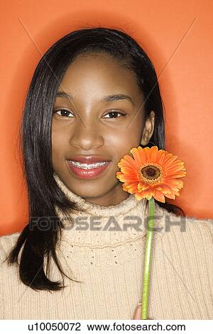 Portrait of smiling African-American teen girl holding single Gerbera Daisy against orange background. View Large Photo Image Stock Image - Portrait of smiling African-American teen girl holding single Gerbera Daisy against orange background.. Fotosearch