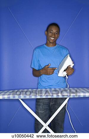 Portrait of smiling African-American teen boy pointing at iron standing at iron board against blue background. View Large Photo Image Stock Image - Portrait of smiling African-American teen boy pointing at iron standing at iron board against blue background.. Fotosearch
