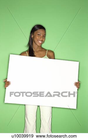 Stock Photo - Portrait of smiling African-American teen girl holding blank white board standing against green background.. Fotosearch