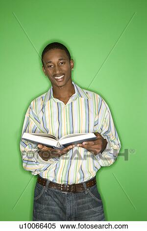 Stock Photography - Portrait of smiling African-American teen boy holding a book standing in front of green background.. Fotosearch